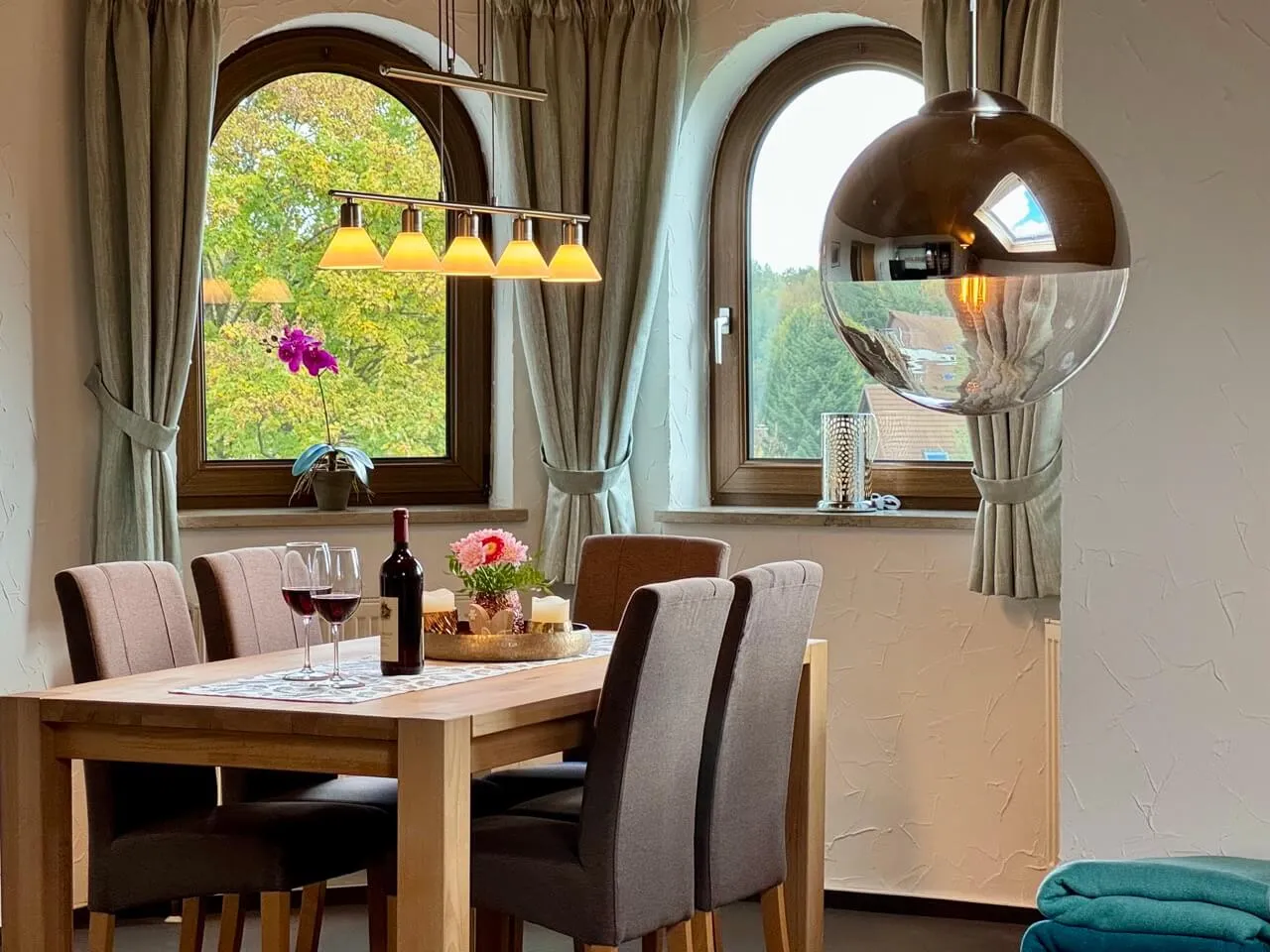 Esstisch am Rundbogenfenster mit Blick auf die Bäume vor dem Haus.