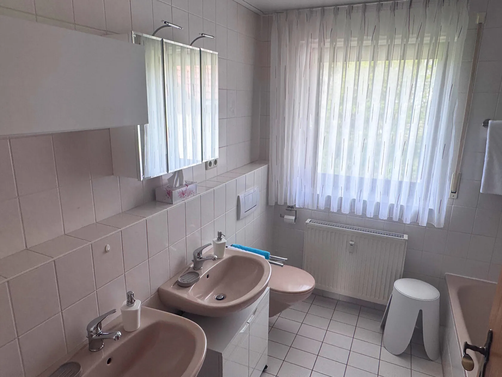 Bad mit zwei Waschbecken, WC und Spiegelschrank am Fenster.