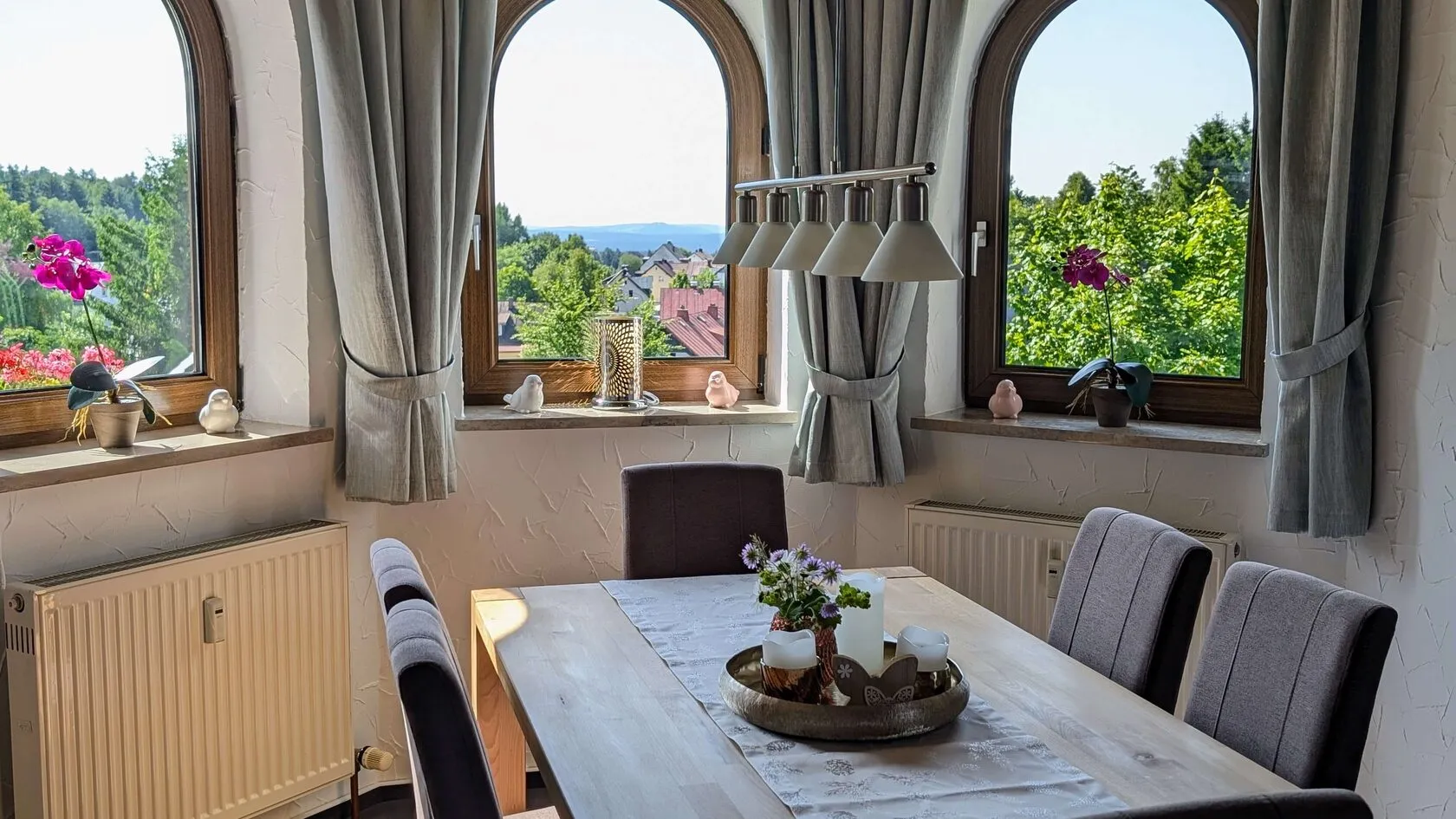 Esstisch vor zwei Rundbogenfenstern mit Blick über das Tal.
