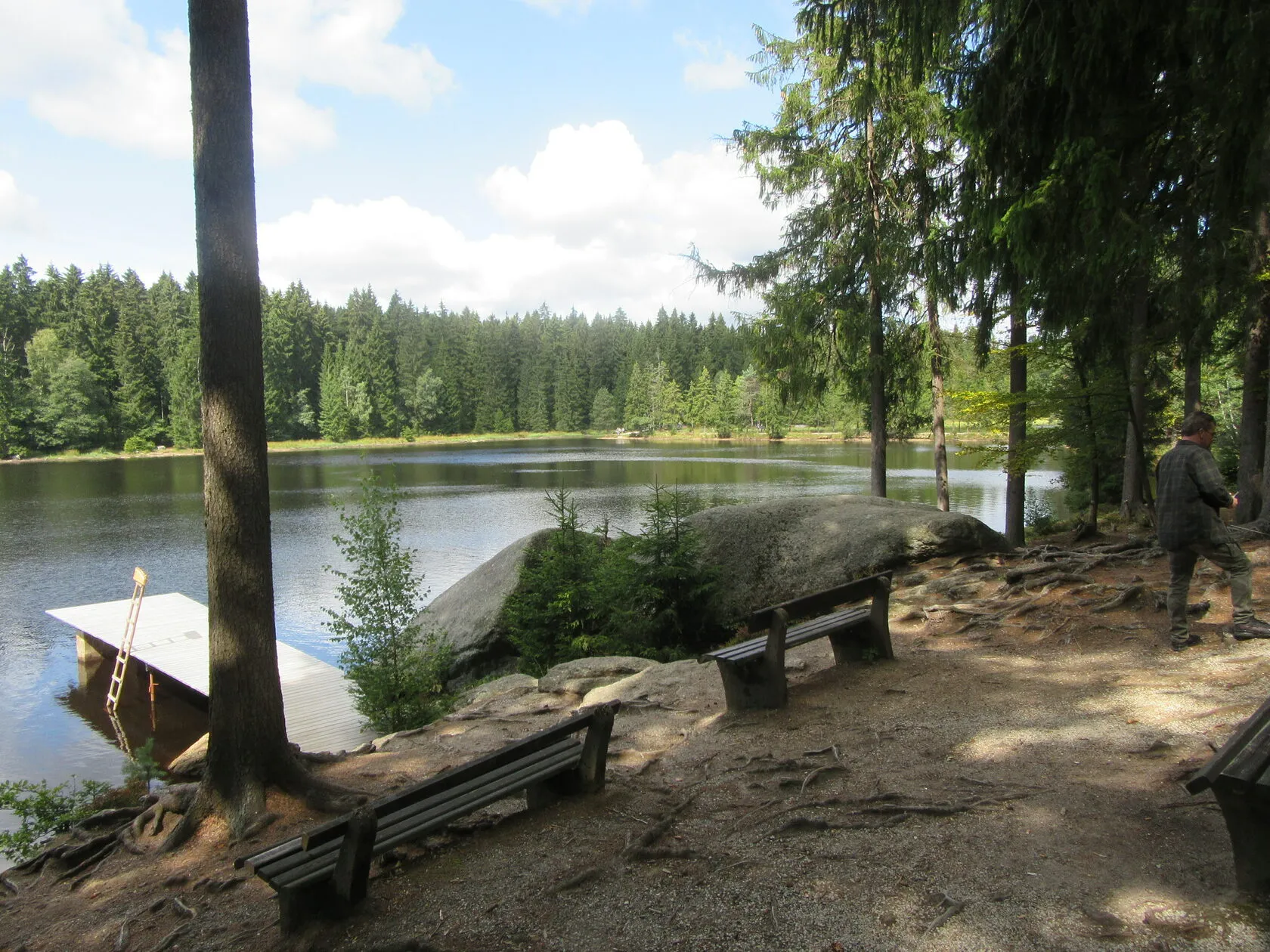 Der Fichtelsee im Sommer, am Ufer Bänke, ein Badesteg und dichter Fichtenwald.