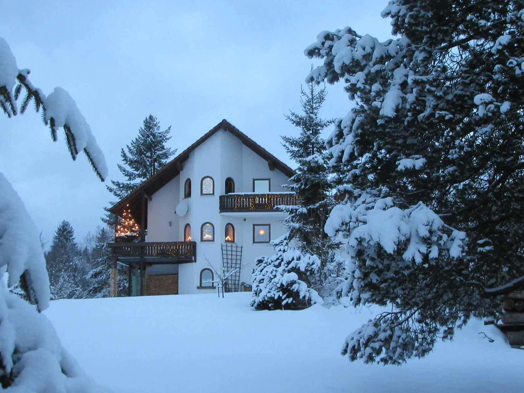 Das verschneite Haus im Winter, der Balkon weihnachtlich beleuchtet.