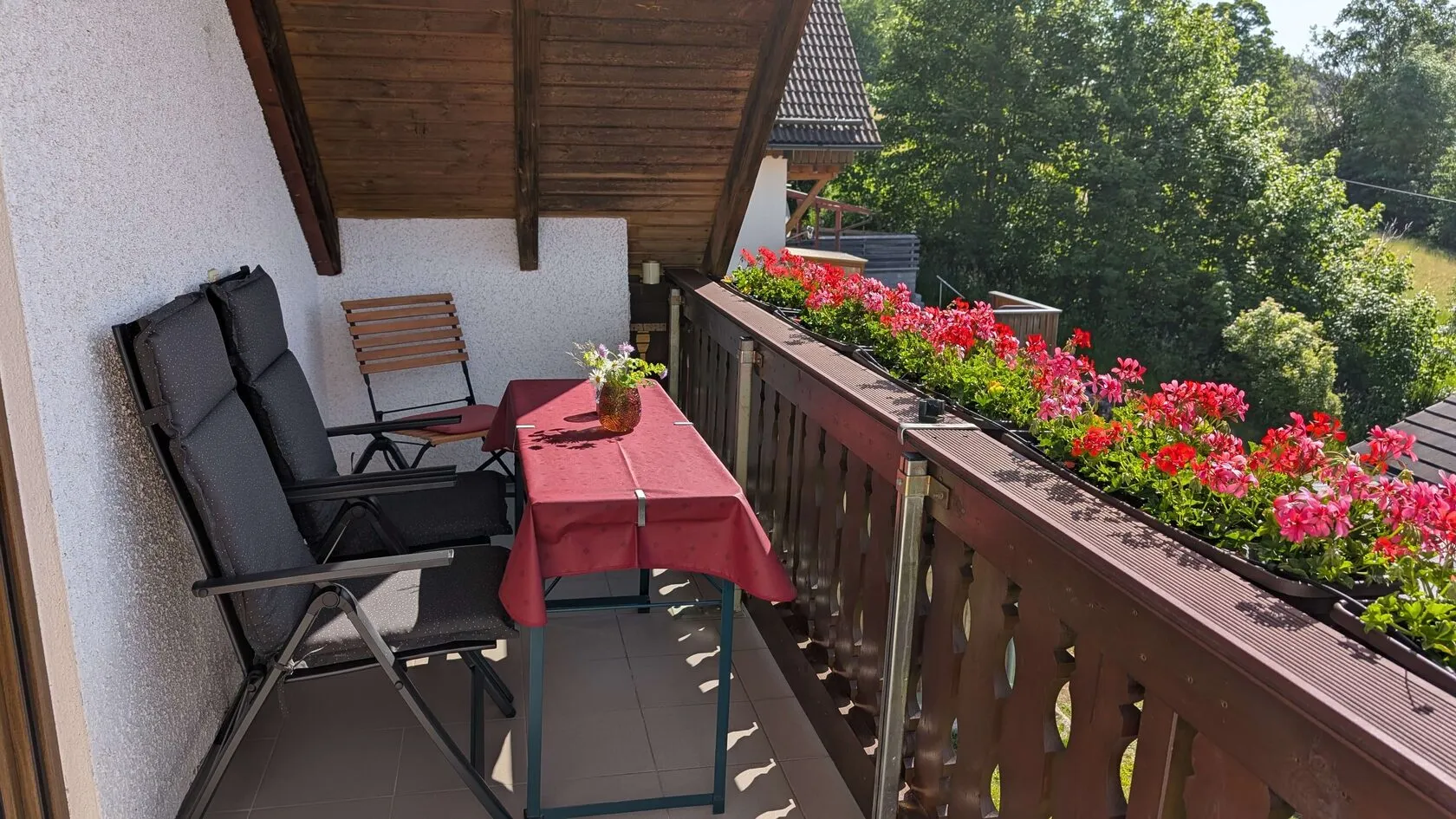 Überdachter Balkon mit Tisch, Stühlen und Geranien am Geländer.