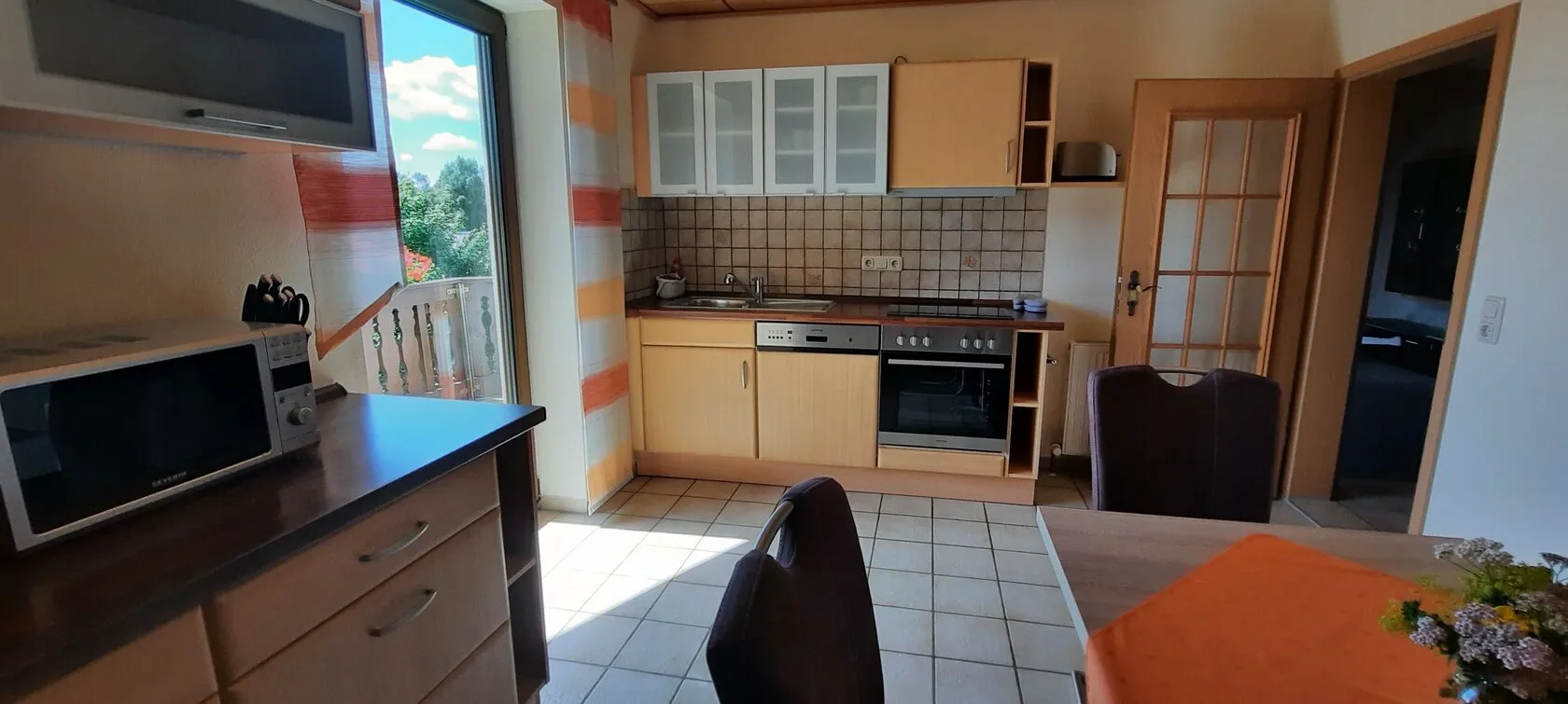 Küche mit Herd, Backofen, Spülmaschine, Mikrowelle und Tür zum Balkon.