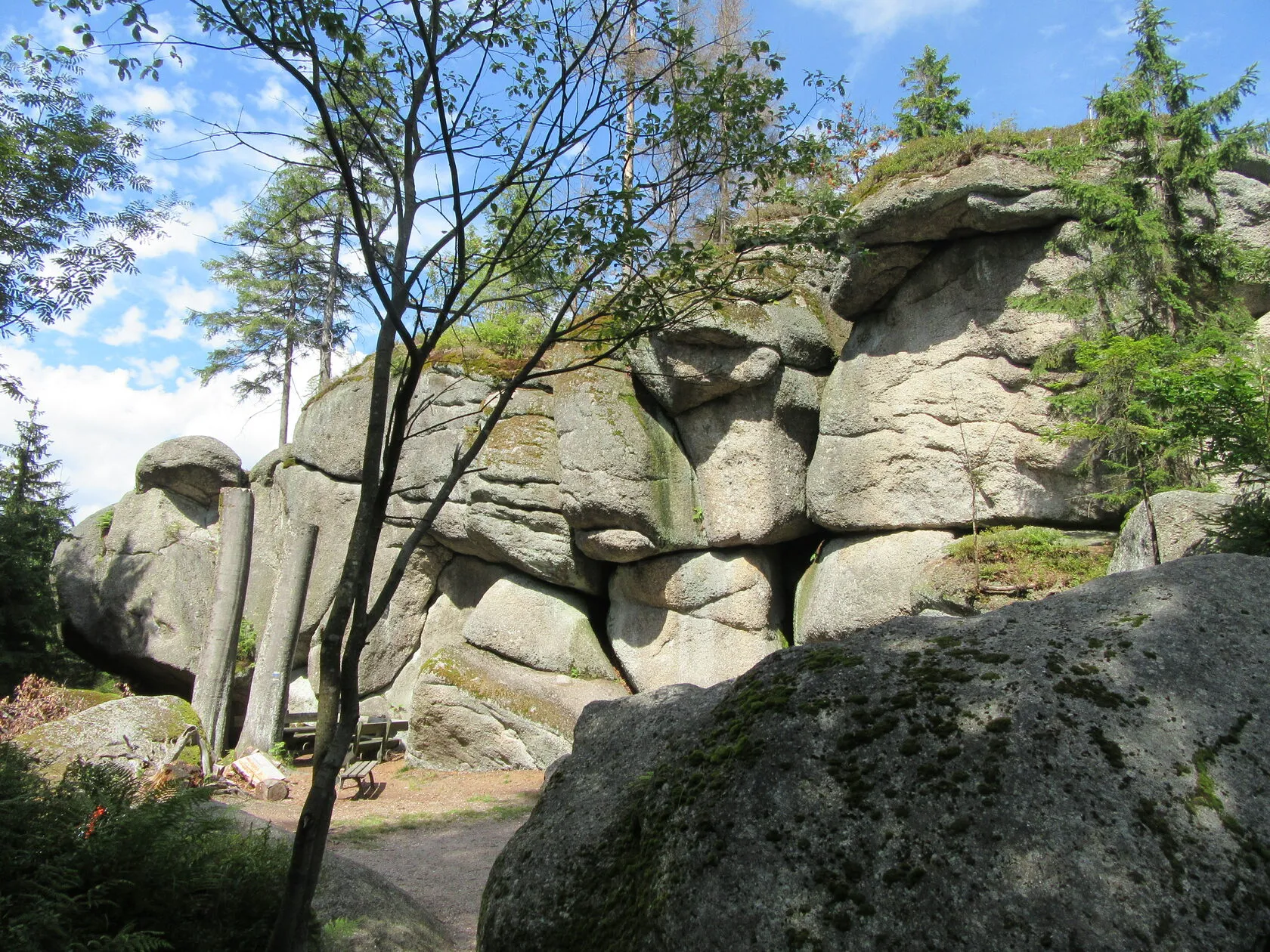 Übereinandergetürmte Granitblöcke unter blauem Himmel, am Fuß der Felsen ein Rastplatz.