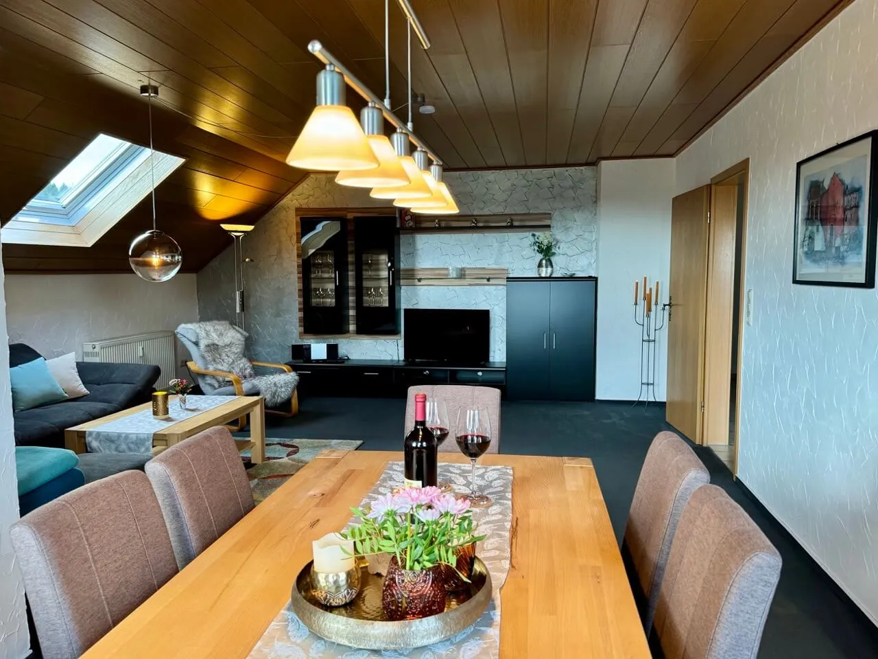 Wohn- und Esszimmer mit großem Holztisch, Sofaecke und Fernseher unter der Holzdecke.