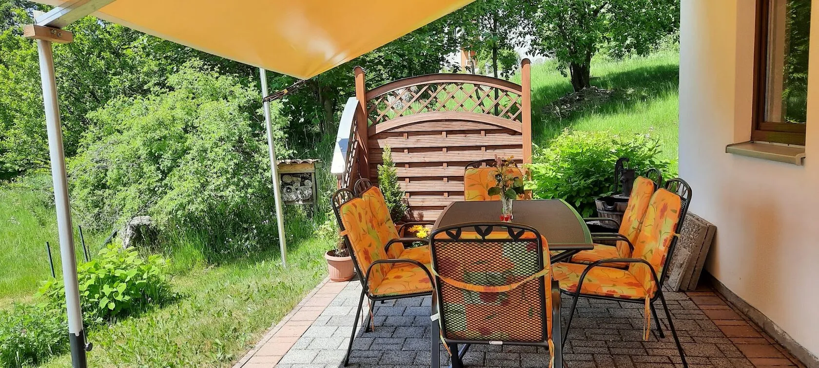 Terrasse mit Gartenmöbeln unter einem Sonnenschirm.